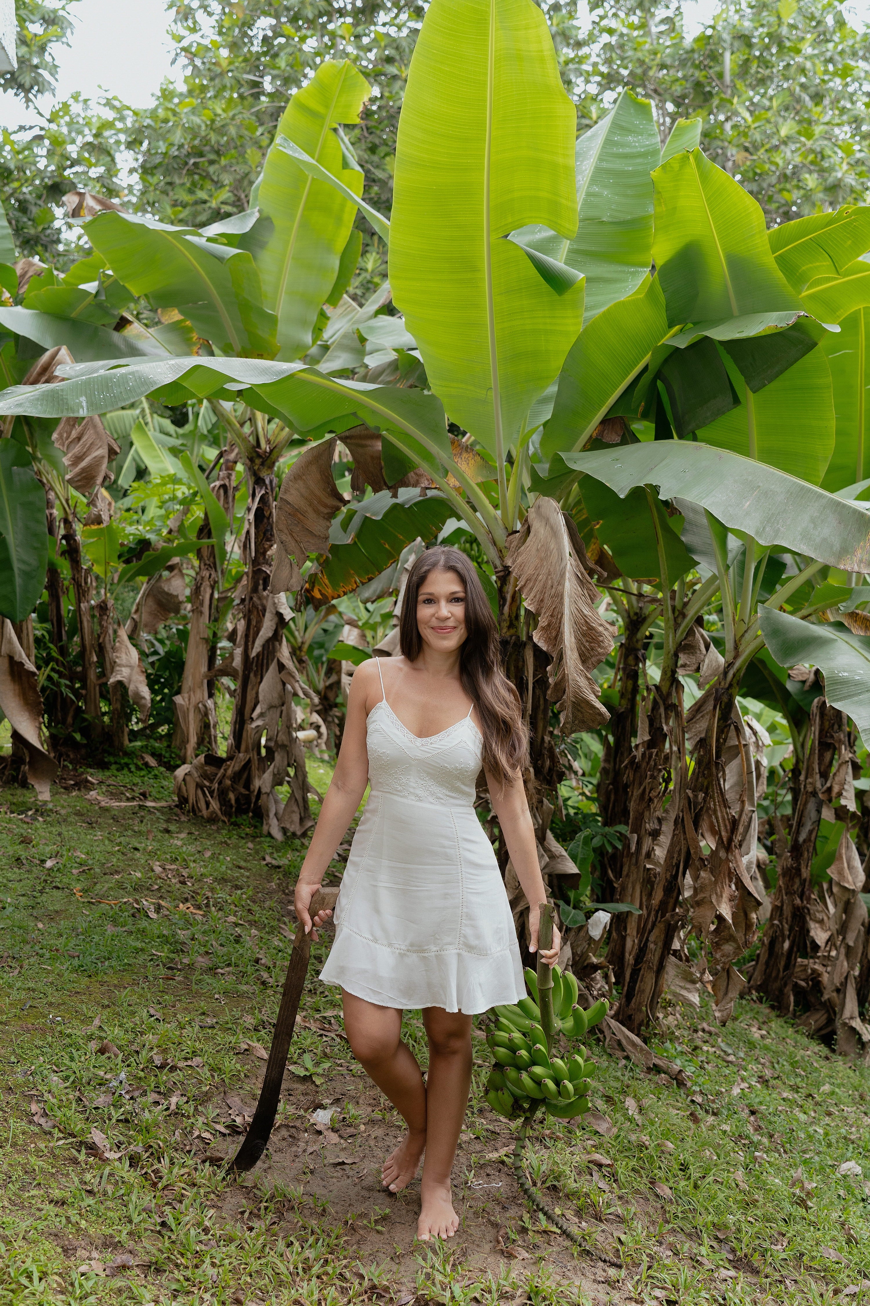 Woman in a white dress holding a machete in a banana plantation
